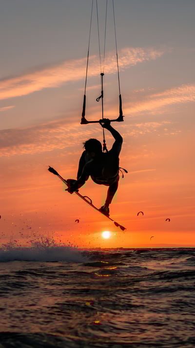 Silhouette eines springenden Kitesurfers bei Sonnenuntergang im baltischen Meer (© Jens Breuer/Getty Images) mobile wallpaper